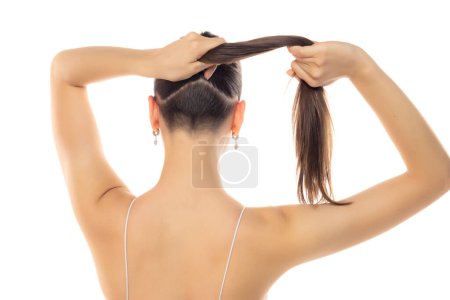 Téléchargez les photos : Vue arrière d'une jeune femme moderne avec tête partiellement rasée et queue de cheval sur fond de studio blanc - en image libre de droit