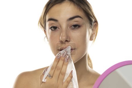 Téléchargez les photos : Jolie jeune femme qui nettoie son visage avec un mouchoir sur fond de studio blanc - en image libre de droit
