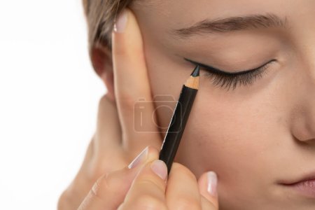 Foto de Mujer aplicando delineador de ojos en el párpado con lápiz sobre un fondo de estudio blanco - Imagen libre de derechos