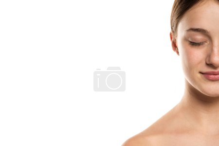 Téléchargez les photos : Demi portrait d'une belle jeune femme souriante aux cheveux attachés les yeux fermés et sans maquillage sur fond de studio blanc. - en image libre de droit