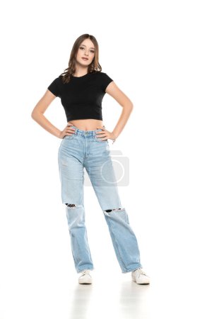 Photo for Young female model wearing ripped jeans and black shirt posing on a white studio background. Front view - Royalty Free Image