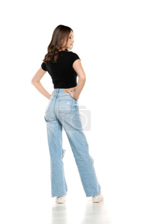 Photo for Young female model wearing ripped jeans and black shirt posing on a white studio background. Back, rear view - Royalty Free Image