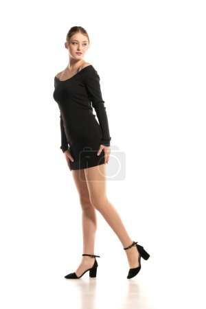 Photo for Summer Chic: Full-Length Portrait of a Young Woman Walking in a Short Dress and Sandals on White Studio Background. Side View. - Royalty Free Image
