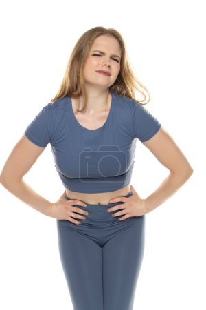 Photo for Young woman in sportswear with pain in her lower abdomen on white studio background - Royalty Free Image