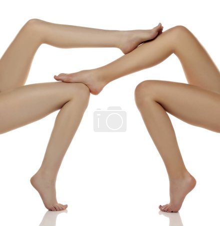 Téléchargez les photos : Deux paires de jambes de belle femme bien entretenues en gros plan sur un fond de studio isolé blanc, Le concept de l'épilation des soins de la peau des pieds - en image libre de droit