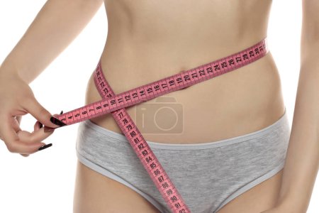 Foto de Mujer mide su cintura con una cinta métrica. Concepto de control de dieta y peso corporal, primer plano, tonificado. Una chica en bragas toma medidas de su figura y pérdida de peso - Imagen libre de derechos