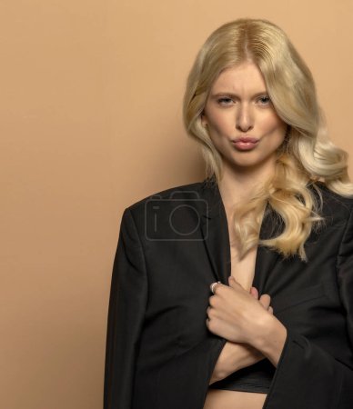 Téléchargez les photos : Beauté portrait de mode jeune modèle avec de longs cheveux blonds poutimg sa bouche sur fond studio beige - en image libre de droit