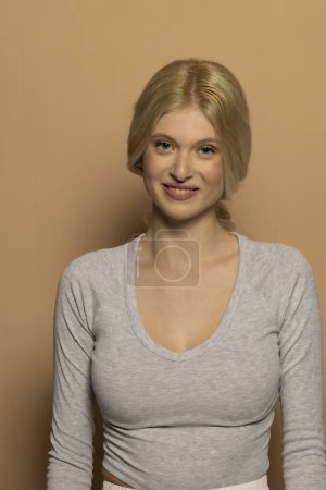 Téléchargez les photos : Portrait de beauté de jeune mannequin souriant aux longs cheveux blonds attachés sur fond de studio beige - en image libre de droit