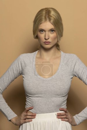 Téléchargez les photos : Portrait de beauté de jeune mannequin avec de longs cheveux blonds attachés sur fond studio beige - en image libre de droit