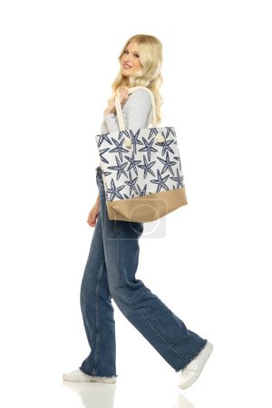 Photo for Beautiful young happy blonde woman in jeans with beach bag on white studio background - Royalty Free Image