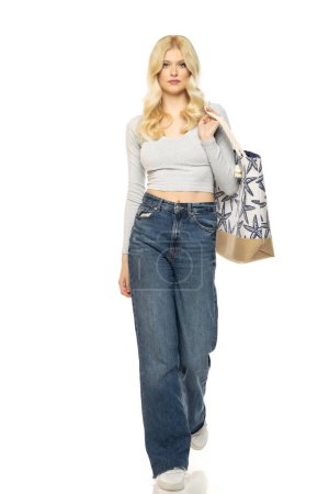 Téléchargez les photos : Belle jeune femme blonde en jeans avec sac de plage sur fond de studio blanc - en image libre de droit