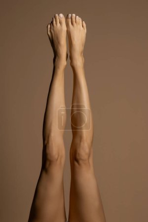 Foto de Desnudo piernas femeninas, vista superior sobre un fondo de estudio beige. - Imagen libre de derechos