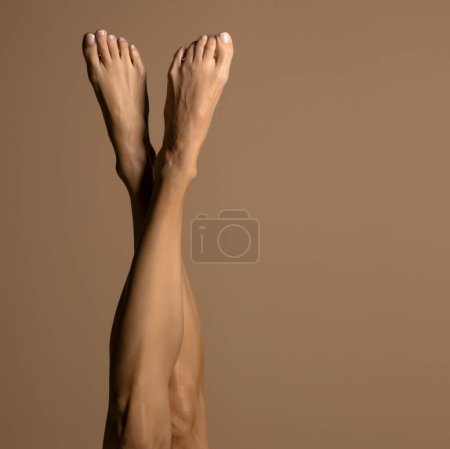 Téléchargez les photos : Jambes féminines nues, vue de dessus sur un fond studio beige. - en image libre de droit