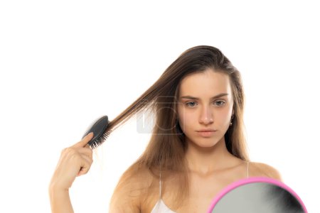 Foto de Una joven se cepilla el pelo en el espejo sobre un fondo blanco de estudio - Imagen libre de derechos