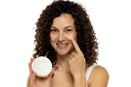 Foto de Retrato de una joven atractiva aplicar un producto de belleza en su cara sobre un fondo de estudio blanco. - Imagen libre de derechos