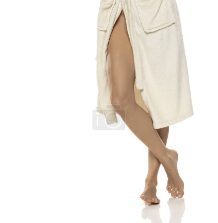 Téléchargez les photos : Jolie femme lisse jambe et genou en peignoir, isolé sur fond de studio blanc. - en image libre de droit