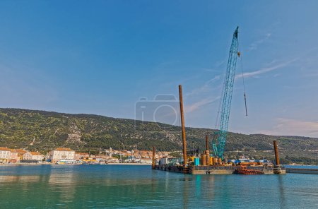 Foto de CRES, CROACIA - 25 de abril de 2020: Construcción de pontones para construcción naval con grúa pequeña frente al puerto del casco antiguo. - Imagen libre de derechos