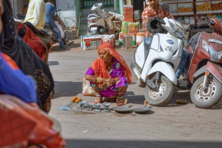 Foto de AJMER, INDIA - MARCH 1 2018: A woman selling metal utensils for food preparation on street market place. - Imagen libre de derechos