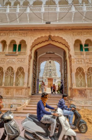 Photo for PUSHKAR, INDIA - MARCH 3 2018: Street view of the Shree Rma Vaikunth Mandir temple entrance at afternoon siesta time with visitors and passers by. - Royalty Free Image