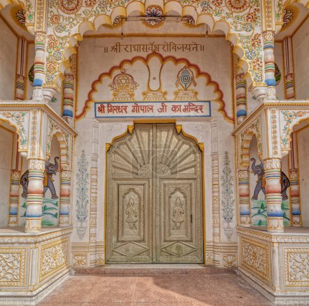 Foto de PUSHKAR, INDIA - MARCH 3 2018: Entrance door with relief detail of a guards guarding the entrance to the Parshuram Dwara Mandir temple. - Imagen libre de derechos