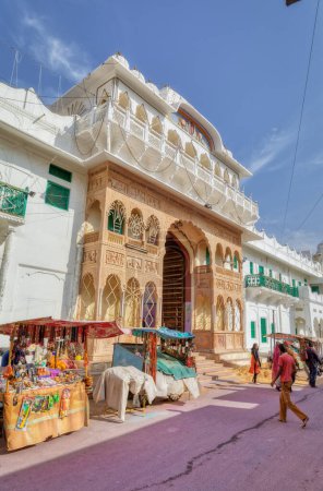 Téléchargez les photos : PUSHKAR, INDIA - MARCH 3 2018: Street view of the Shree Rma Vaikunth Mandir temple entrance at afternoon siesta time with visitors and passers by. - en image libre de droit