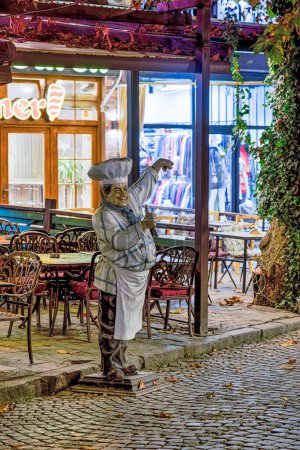Photo for PRIZREN, KOSOVO - NOVEMBER 12, 2022: A plastic chef and menu holder inviting guests at the entrance to the restaurant in historic city center. long exposure - Royalty Free Image