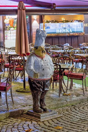Photo for PRIZREN, KOSOVO - NOVEMBER 12, 2022: A plastic chef and menu holder inviting guests at the entrance to the restaurant in historic city center. long exposure - Royalty Free Image