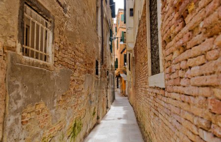 Photo for A narrow Venetian alley lined with time-weathered brick walls, exuding the enchanting allure of old-world architecture. - Royalty Free Image