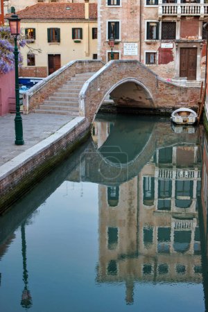 Foto de Majestuosa vista del puente Ponte San Boldo en Venecia, reflejada en el canal suavemente ondulado con un edificio antiguo en el fondo. - Imagen libre de derechos