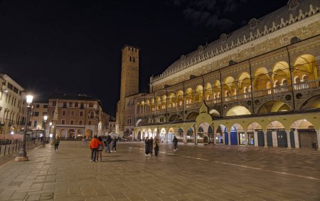 Foto de PADUA, ITALIA - 03 ABRIL 2023: Escena nocturna con gente paseando bajo la luz de la luna en la Piazza della Frutta dominada por el Palazzo della Ragione. - Imagen libre de derechos