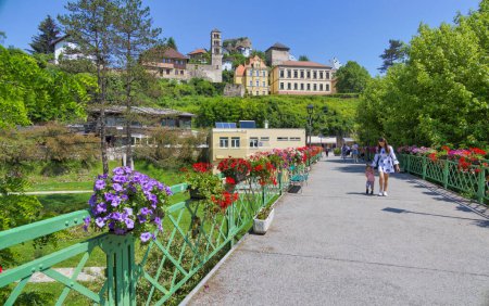 Téléchargez les photos : JAJCE, BOSNIE-HERZÉGOVINE - 2 juin 2023 : Piétons traversant le pont Ajfel au-dessus de la rivière Pliva, décorés de diverses fleurs, avec vue sur la forteresse et la vieille ville. - en image libre de droit