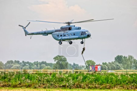 Photo for VARAZDIN, CROATIA - July 21, 2018: Croatian military Mil Mi-8 helicopter flies with a special police officer dangling from a rope during an airshow. - Royalty Free Image