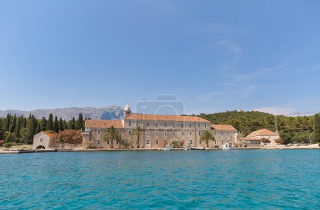Téléchargez les photos : KORCULA, CROATIE - 24 juin 2019 : Vue panoramique depuis la mer, mettant en évidence le monastère franciscain Badija sur l'île du même nom. - en image libre de droit