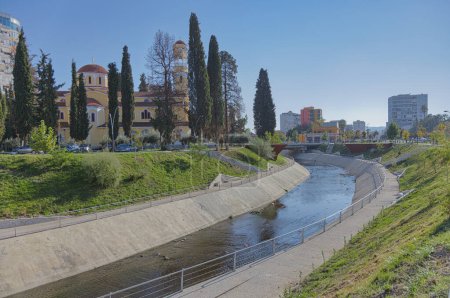 Téléchargez les photos : FIER, ALBANIE - 20 octobre 2022 : Vue panoramique du canal manucuré par lequel coule la rivière Gjanica à côté de la cathédrale orthodoxe Saint-Georges de Fier. - en image libre de droit