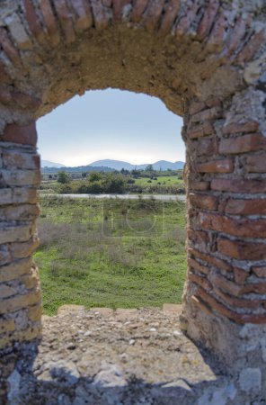 Foto de Una vista serena del paisaje más allá de las paredes del castillo triangular veneciano en Butrint, destacando la fusión de la belleza medieval y natural. - Imagen libre de derechos