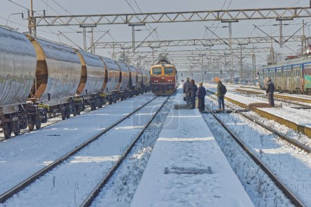 Téléchargez les photos : DUGO SELO, CROATIE - 25 janvier 2023 : Locaux près d'un train enneigé à la gare de Dugo Selo par une belle journée d'hiver. - en image libre de droit