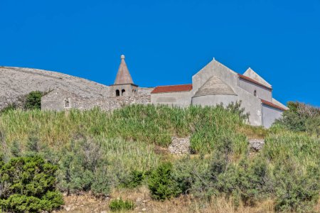 Téléchargez les photos : Ancienne église avec un clocher en forme de cône au milieu d'arbustes méditerranéens sur l'île de Pag. - en image libre de droit