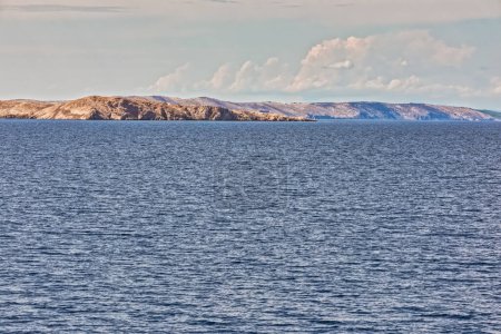 Téléchargez les photos : Eaux calmes de la mer Adriatique avec une vue lointaine sur le littoral accidenté des îles Pag sous un ciel nuageux doux. - en image libre de droit