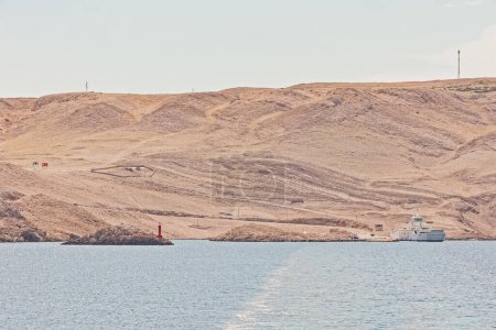 Foto de Zigljen, Pag Island, Croacia - 2 de septiembre de 2020: El ferry Jadrolinija en el puerto, listo para transportar a los visitantes contra un fondo estéril de la colina. - Imagen libre de derechos