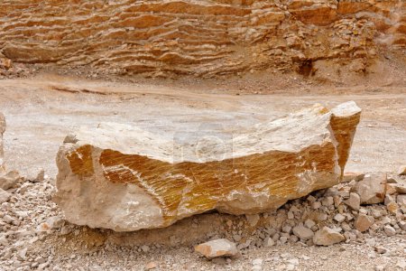 Téléchargez les photos : Un grand rocher calcaire reposant sur du gravier avec des murs de carrière en arrière-plan. - en image libre de droit