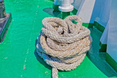Foto de Primer plano de una cuerda marítima enrollada ordenada cuidadosamente en la vibrante cubierta verde de un ferry. - Imagen libre de derechos