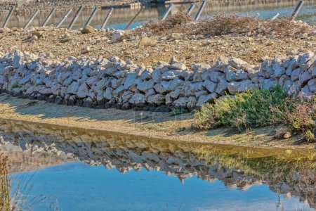 Foto de Vista de cerca de un muro de piedra tradicional y su reflejo en las tranquilas aguas de las salinas Solana Pags. - Imagen libre de derechos