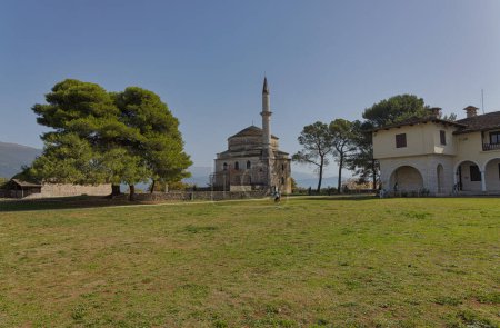 Téléchargez les photos : IOANNINA, GRÈCE - 17 août 2023 : Visiteurs explorant la mosquée historique Fethiye avec son minaret distinctif, nichée dans le paysage luxuriant d'Ioannina. - en image libre de droit