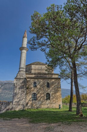Téléchargez les photos : IOANNINA, GRÈCE - 23 octobre 2023 : La mosquée historique Fethiye se dresse avec son impressionnant minaret au milieu de la verdure sous le ciel bleu clair à Ioannina. - en image libre de droit