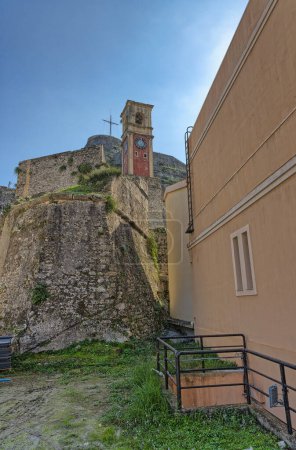 Téléchargez les photos : CORFU, GRÈCE - 21 octobre 2022 : La tour de l'horloge historique debout sur la toile de fond de la vieille forteresse de Corfou sous un ciel bleu clair. - en image libre de droit