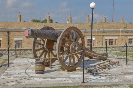 Foto de CORFU, GRECIA - 21 de octubre de 2022: Un cañón antiguo sobre ruedas de madera expuesto en la antigua fortaleza de Corfú, sobre el telón de fondo de edificios históricos. - Imagen libre de derechos