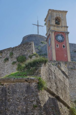 Téléchargez les photos : CORFU, GRÈCE - 21 octobre 2022 : L'emblématique tour de l'horloge rouge de la vieille forteresse de Corfou se dresse comme une sentinelle au-dessus des murs historiques sous un ciel clair. - en image libre de droit