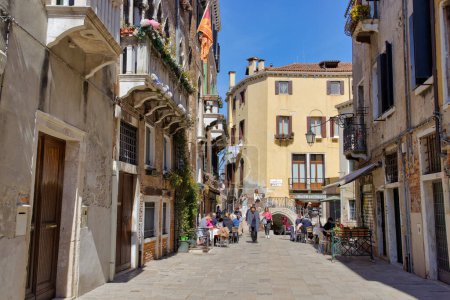 Téléchargez les photos : VENISE, ITALIE - 10 AVRIL 2023 : Les habitants et les touristes se promènent dans des cafés pittoresques le long d'un canal serein dans le cœur historique de Venices. - en image libre de droit