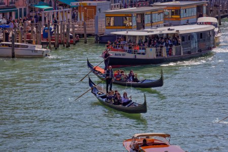 Foto de VENECIA, ITALIA - 10 DE ABRIL DE 2023: Un barco que transporta turistas pasando por hermosas fachadas de casas antiguas que bordean el Gran Canal. - Imagen libre de derechos