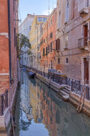 Photo for VENICE, ITALY - APRIL 10 2023: A narrow Venetian canal flanked by age-old buildings, with daylight casting a soft glow on the structure at the end. - Royalty Free Image